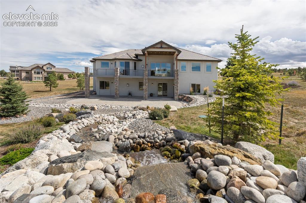 Image 46 of 50: Stucco exterior with stone accents, multiple balconies, a lower-level patio