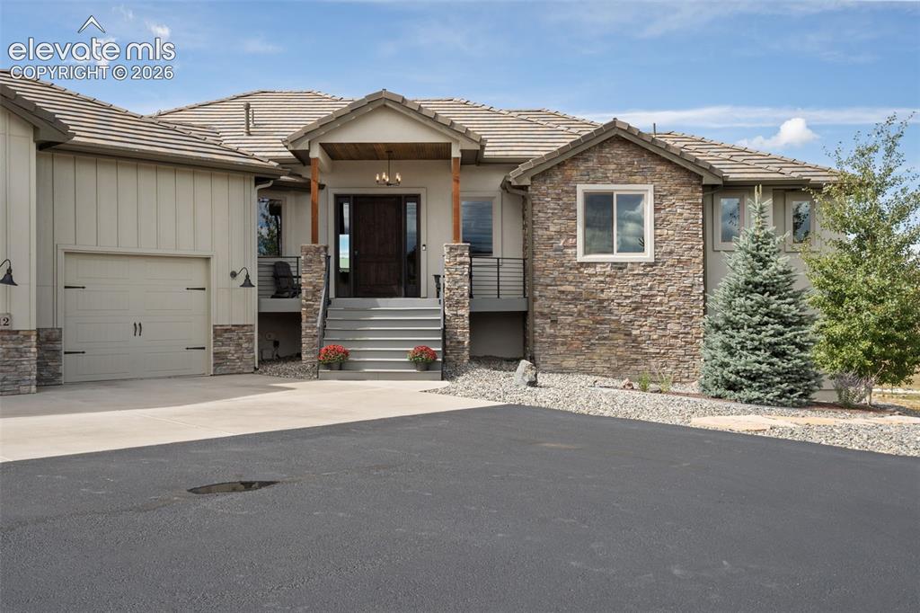 Image 5 of 50: Stone facade accents, covered entry with wood columns, tile roof, attached 