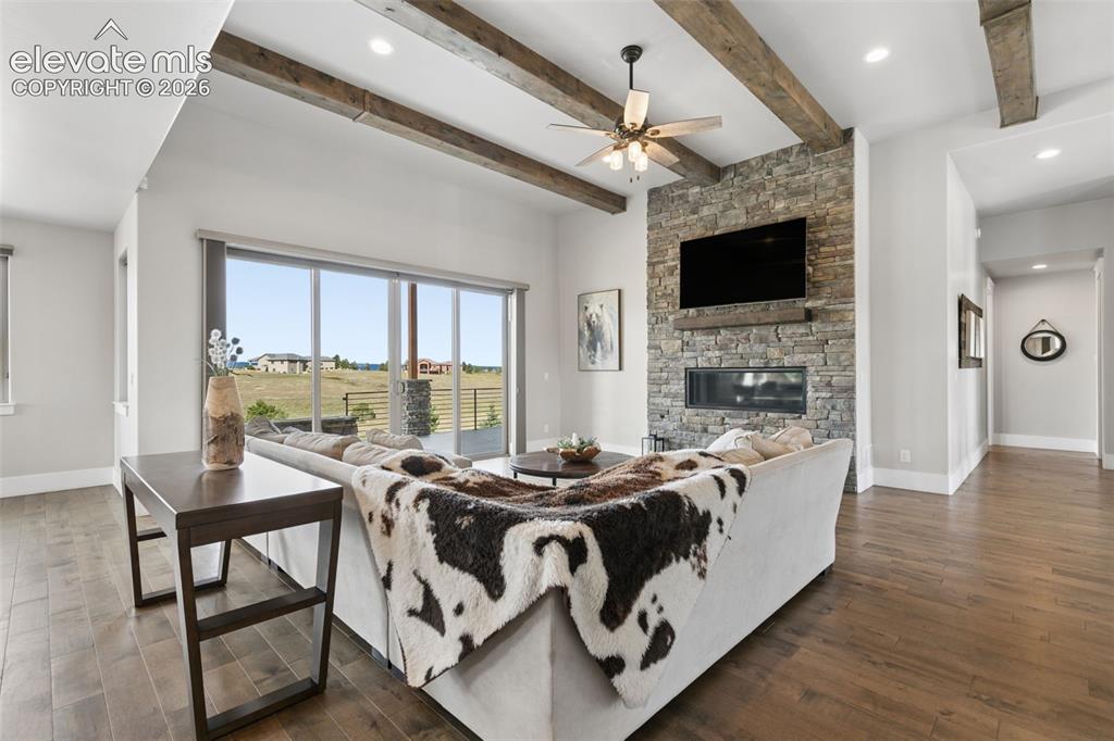 Image 8 of 50: Living area with wood-finish flooring, exposed ceiling beams, and a stone-c