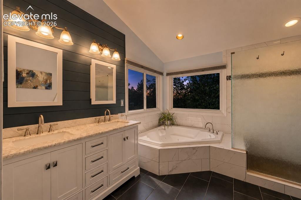 Image 24 of 50: Bathroom featuring a double vanity with stone countertops, a corner jetted
