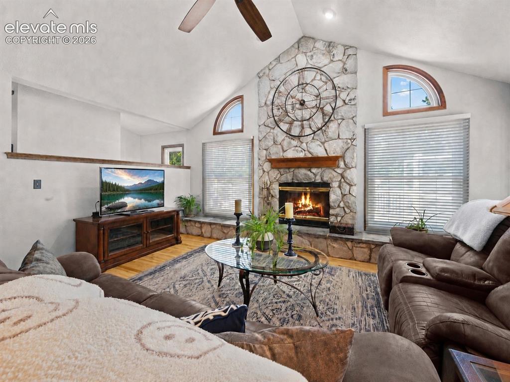 Image 3 of 50: Vaulted ceiling with a ceiling fan, stone-clad fireplace with a wood mantle