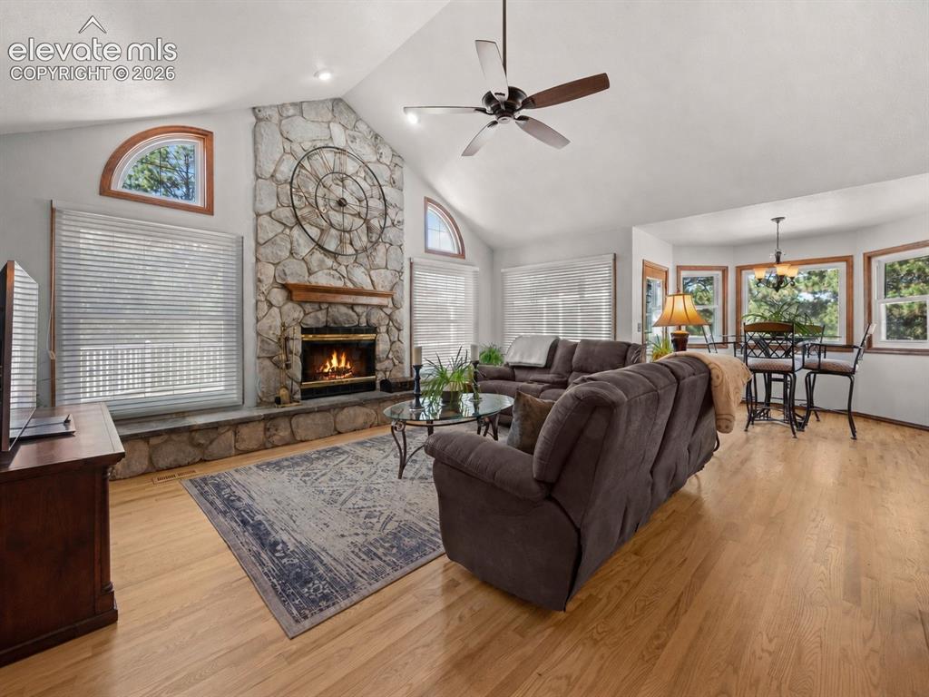 Image 4 of 50: Vaulted ceiling with a ceiling fan, stone-clad fireplace, wood-finish floor