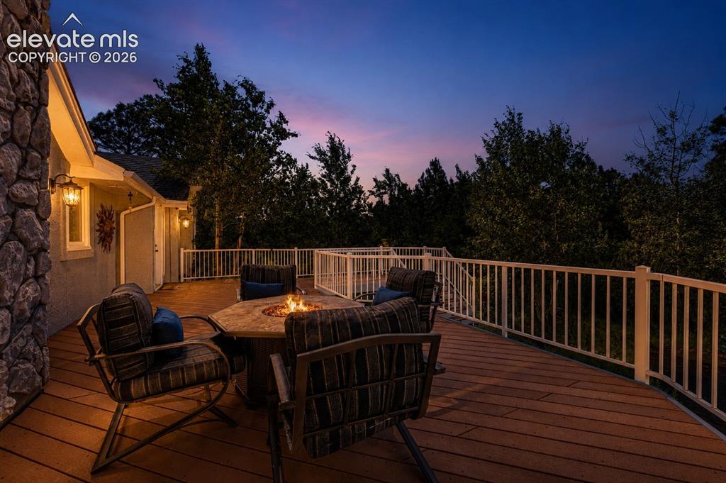 Image 40 of 50: Expansive wood-finish deck featuring a built-in stone fire pit, white picke