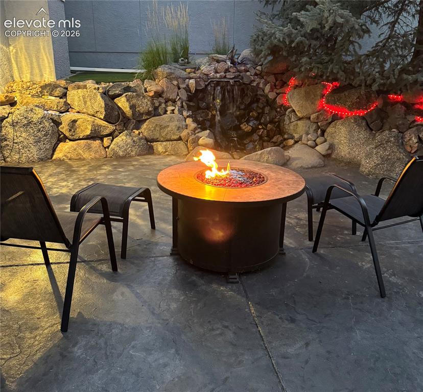 Image 46 of 50: Stamped concrete patio with a built-in fire pit, surrounded by a rock retai