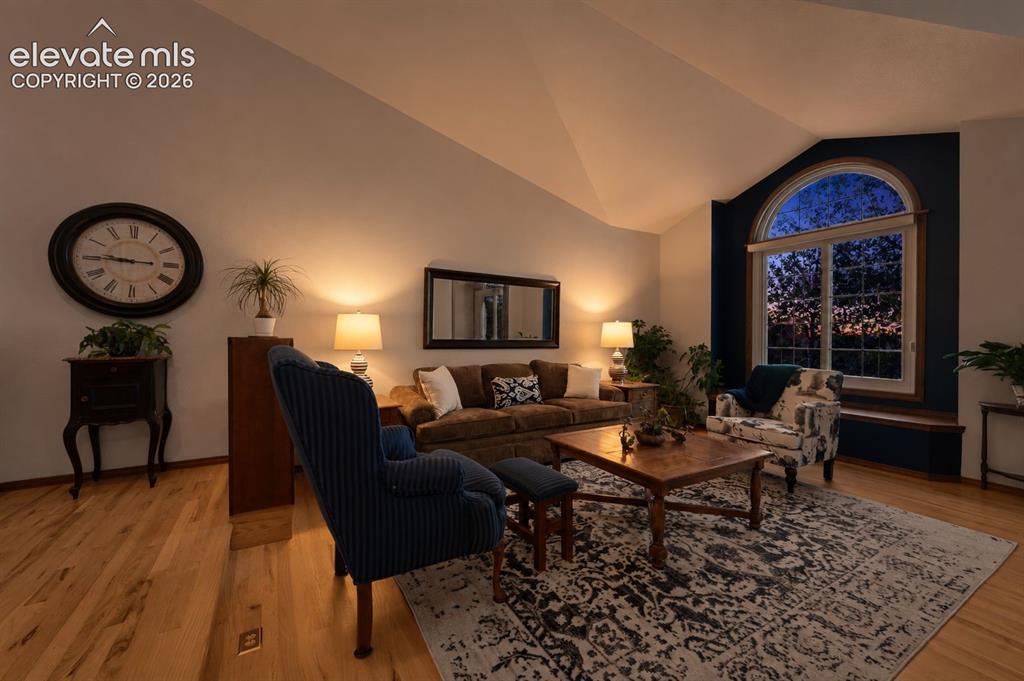 Image 8 of 50: Living room featuring an arched picture window, vaulted ceiling, and hardwo