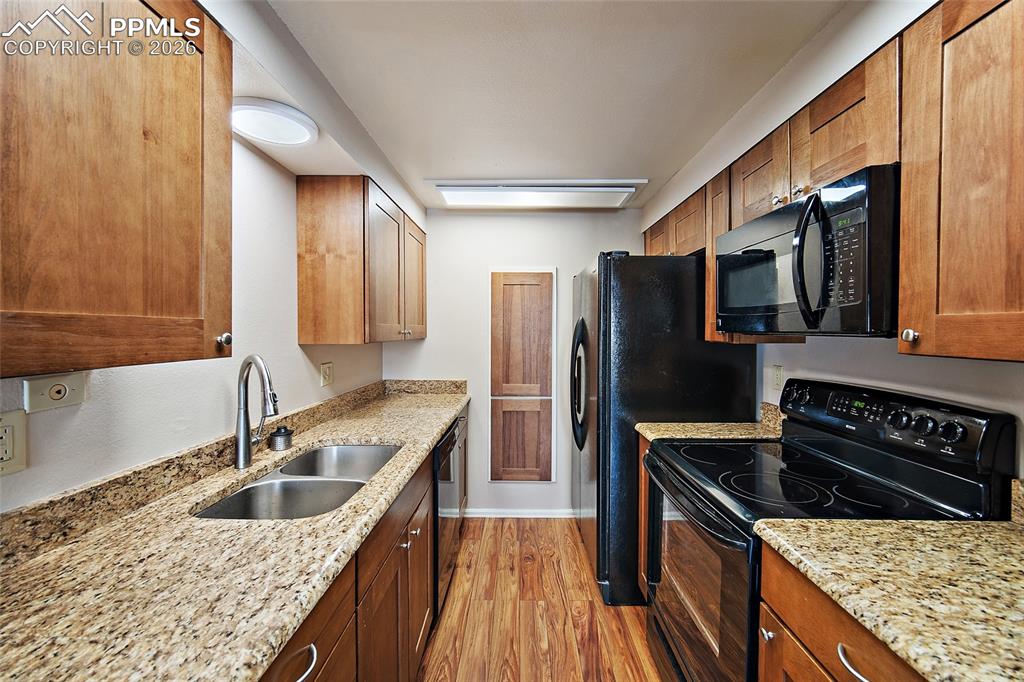 Image 11 of 31: Kitchen featuring black appliances, light wood-style floors, light stone co