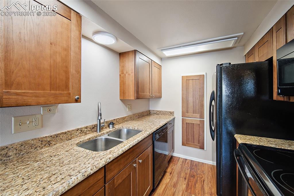Image 12 of 31: Kitchen featuring black appliances, light stone countertops, light wood-sty