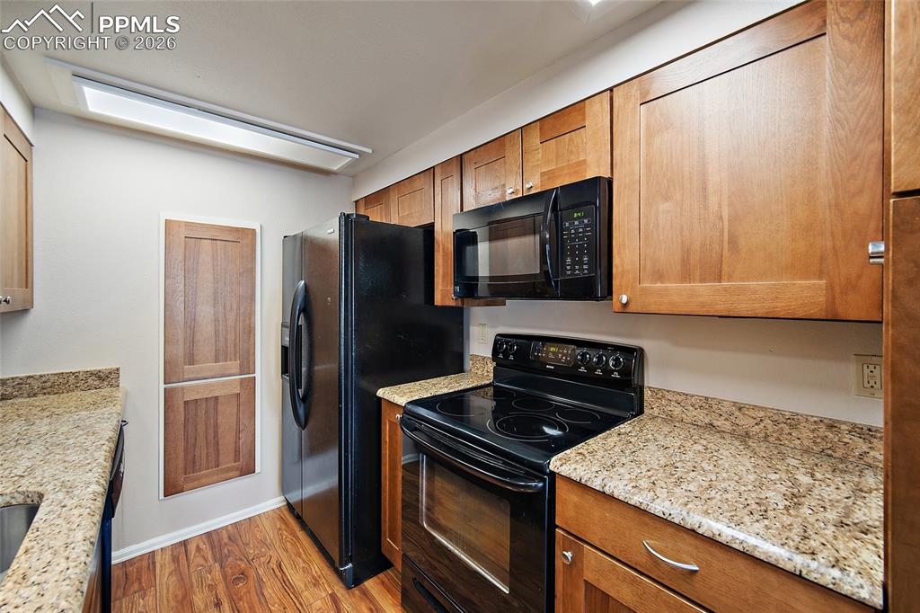 Image 13 of 31: Kitchen featuring black appliances, light wood-style floors, light stone co