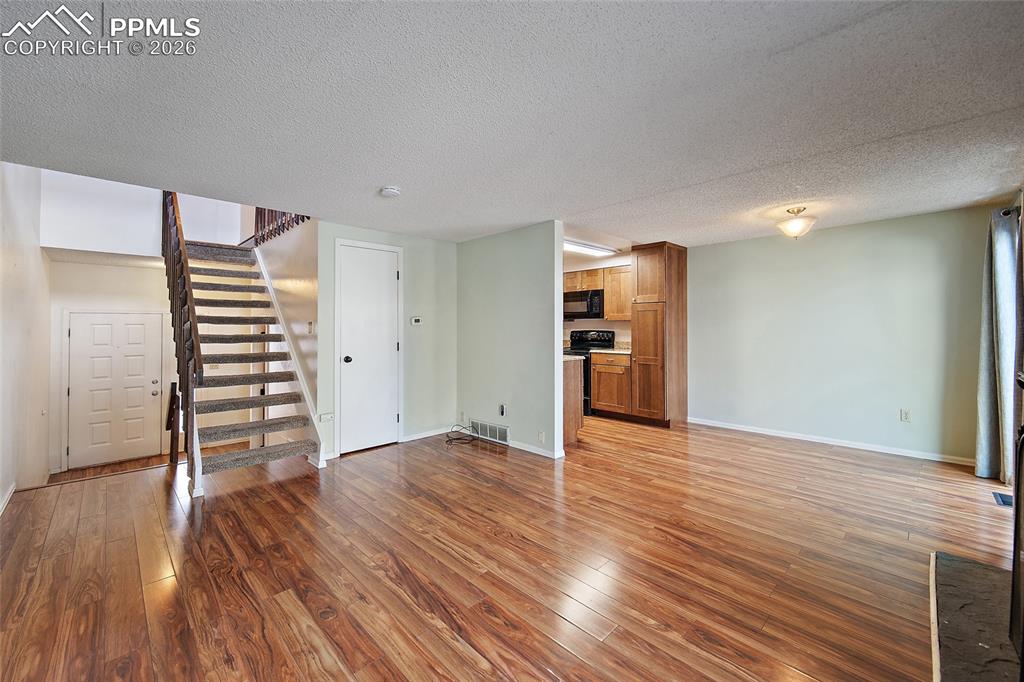Image 9 of 31: Unfurnished living room with a textured ceiling and dark wood-style floors