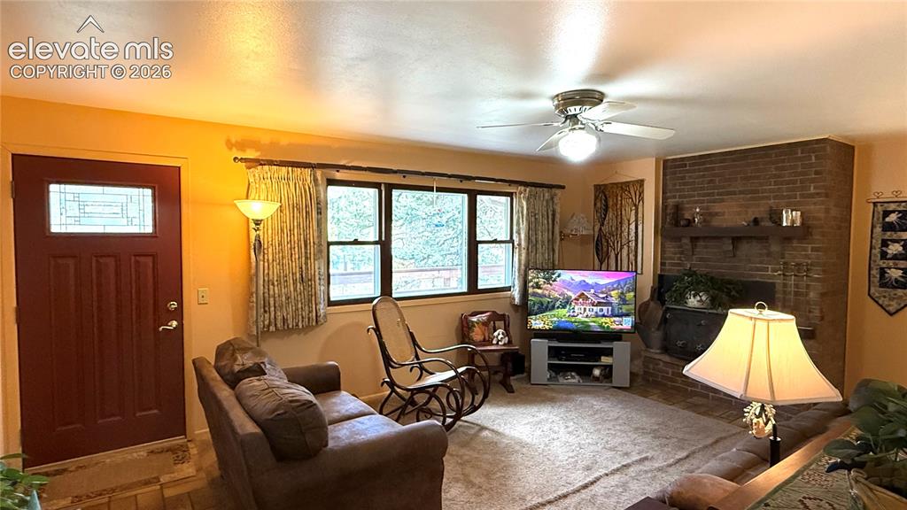 Image 2 of 38: Living area featuring a brick fireplace with wood mantel, multiple windows,