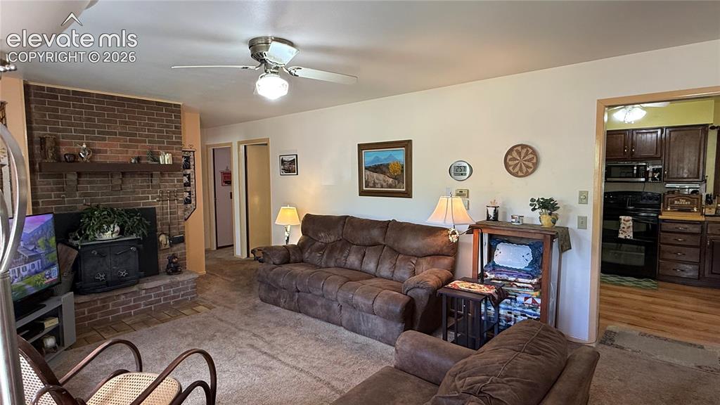 Image 3 of 38: Living space featuring a brick fireplace with a wood mantle, a ceiling fan