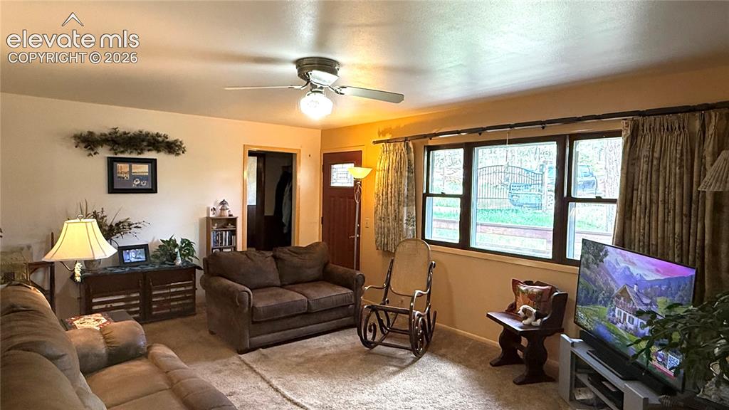 Image 4 of 38: Spacious living area featuring neutral carpeting, a ceiling fan with integr