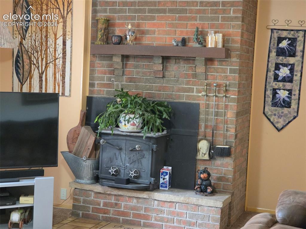 Image 5 of 39: Brick fireplace featuring a wood-burning stove, raised hearth, and wood man