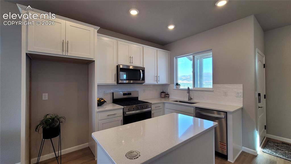 Image 8 of 41: Kitchen with Quartz countertops, island, stainless steel gas range, microwa
