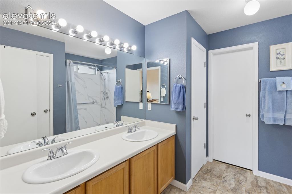 Image 16 of 32: Dual sinks set in a white countertop, wood-finish cabinetry, a large vanity