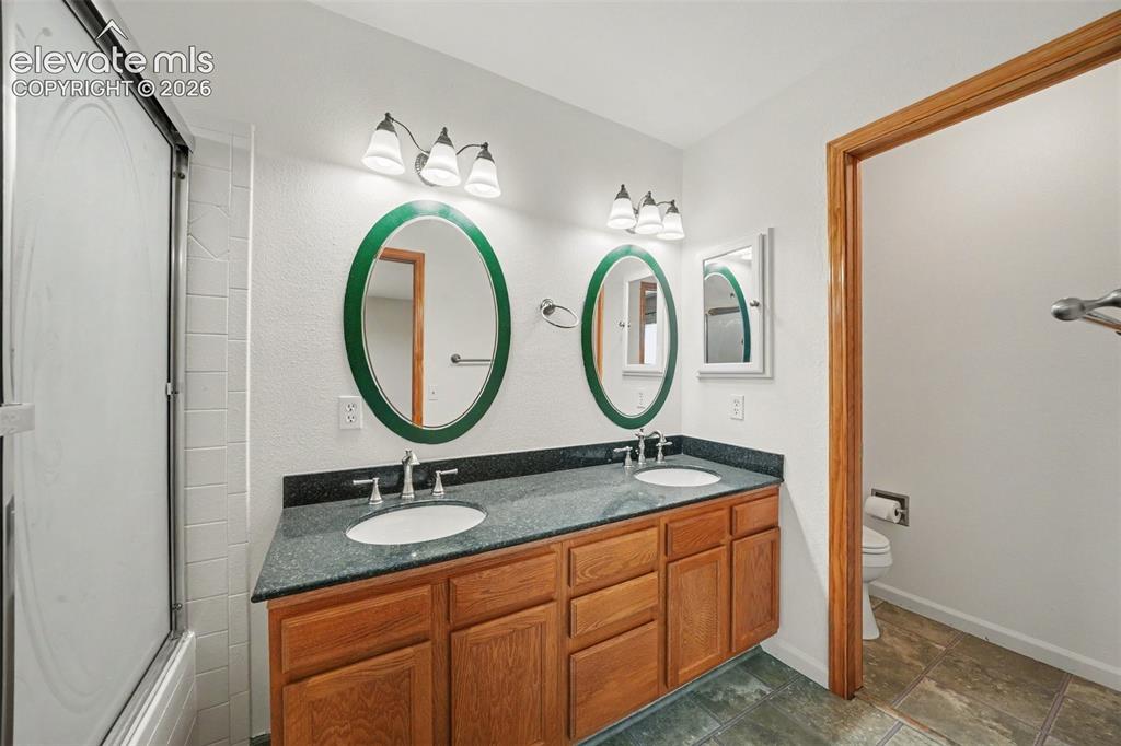 Image 11 of 23: Dual basin vanity with wood-finish cabinetry and dark countertop