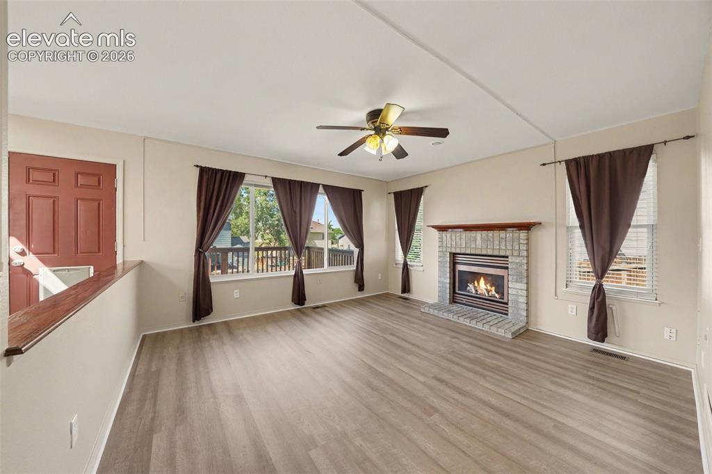 Image 6 of 23: Spacious living area featuring wood-finish flooring, a stone-surround firep