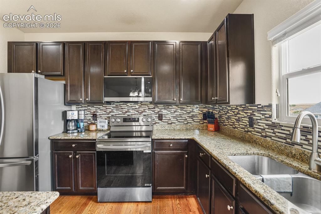 Image 20 of 44: Kitchen featuring dark wood cabinetry, stainless steel appliances, granite 