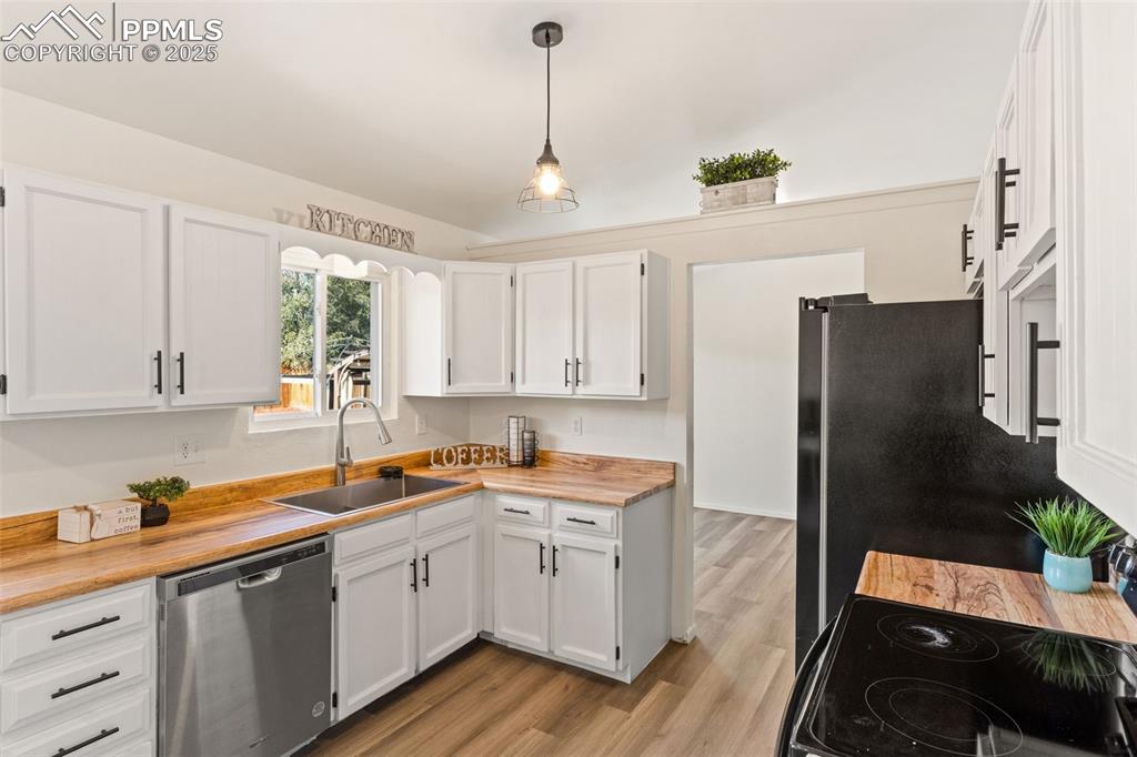 Image 19 of 44: Kitchen with wood counters, stainless steel dishwasher, white cabinetry, an