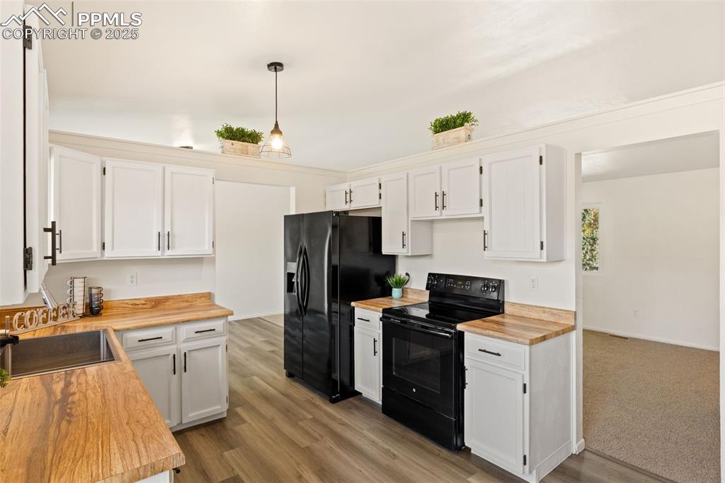 Image 20 of 44: Kitchen with black appliances, white cabinets, wooden counters, and decorat