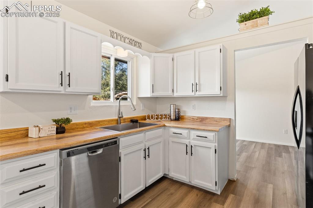 Image 21 of 44: Kitchen with stainless steel dishwasher, white cabinetry, dark wood finishe