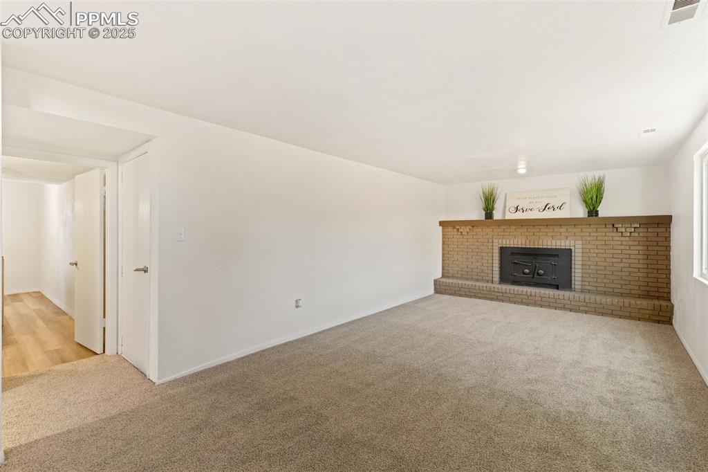 Image 24 of 44: Unfurnished living room with light colored carpet and a brick fireplace