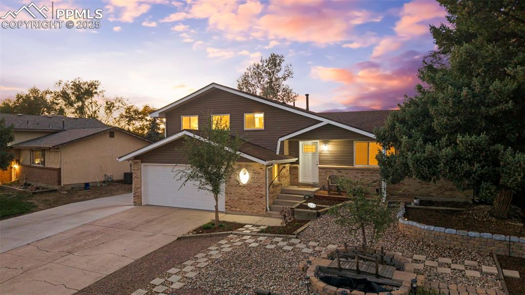 Image 4 of 44: View of front of house with a fire pit, concrete driveway, brick siding, an