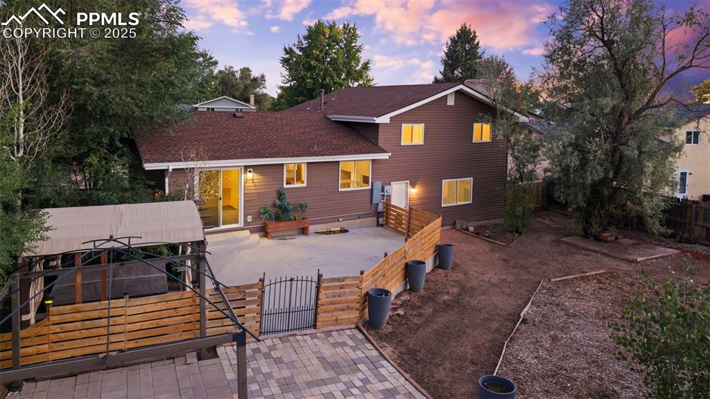 Image 5 of 44: Back of property at dusk featuring a patio, a gate, and roof with shingles