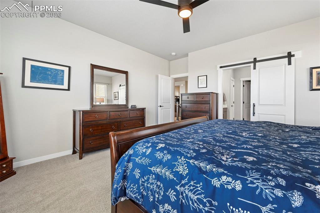 Image 20 of 49: Primary Bedroom Carpeted with a barn door and ceiling fan