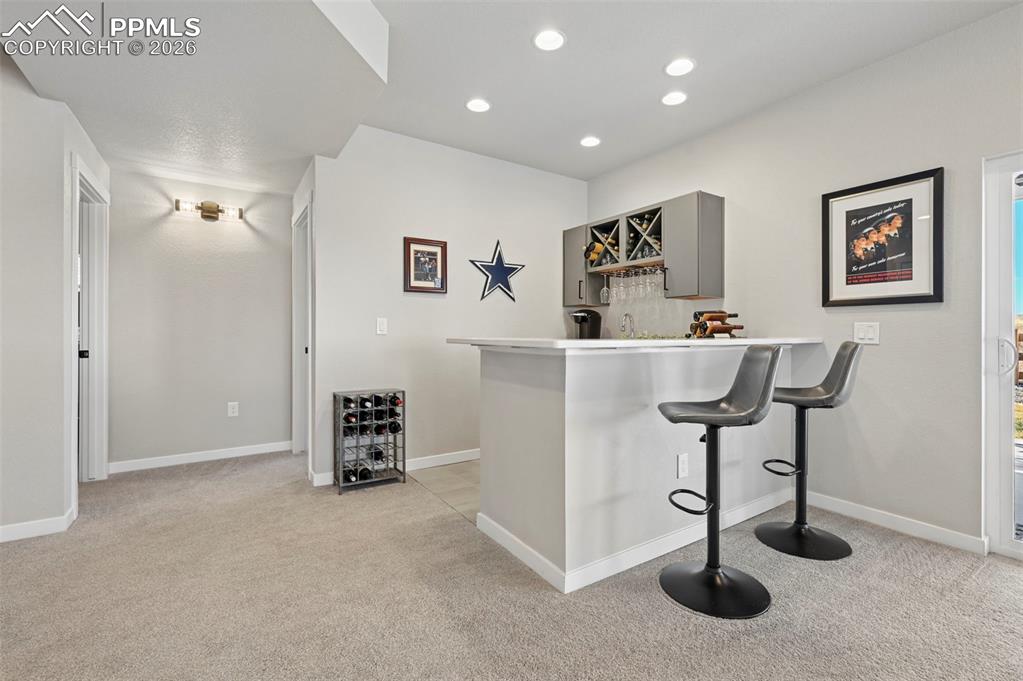 Image 32 of 49: Indoor bar with light countertops, light carpet, gray cabinetry, and recess
