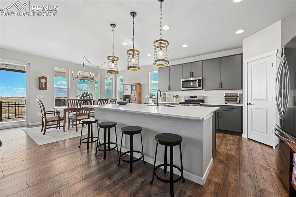 Image 7 of 49: Kitchen featuring gray cabinetry, a kitchen island with sink, a breakfast b