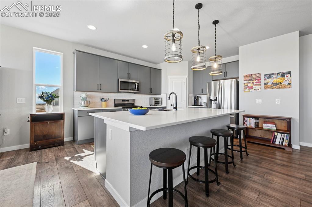 Image 9 of 49: Kitchen featuring gray cabinets, a breakfast bar, an island with sink, deco