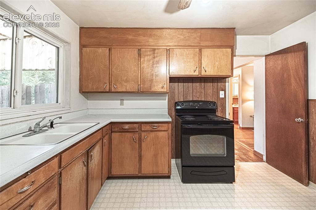 Image 12 of 44: Kitchen featuring wood cabinetry, a double basin sink, black range, and whi