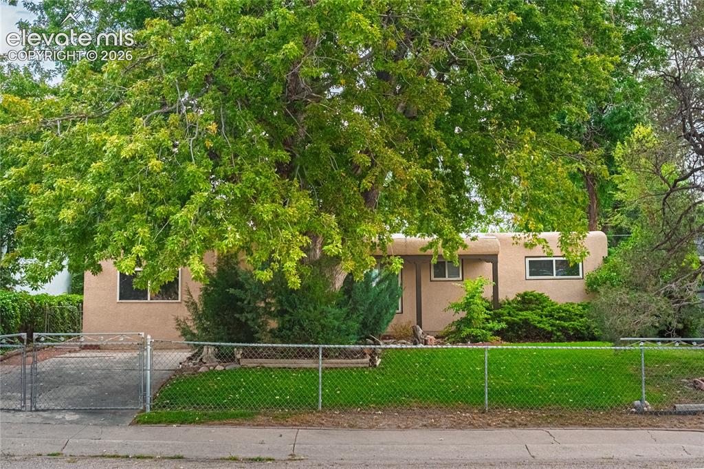 Image 38 of 44: Stucco exterior residence with mature trees and a chain-link fence