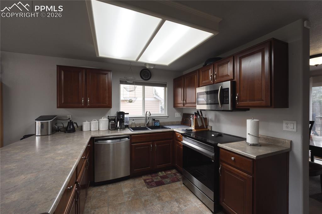 Image 14 of 45: U-shaped kitchen featuring wood cabinetry, stone-finish countertops, and st