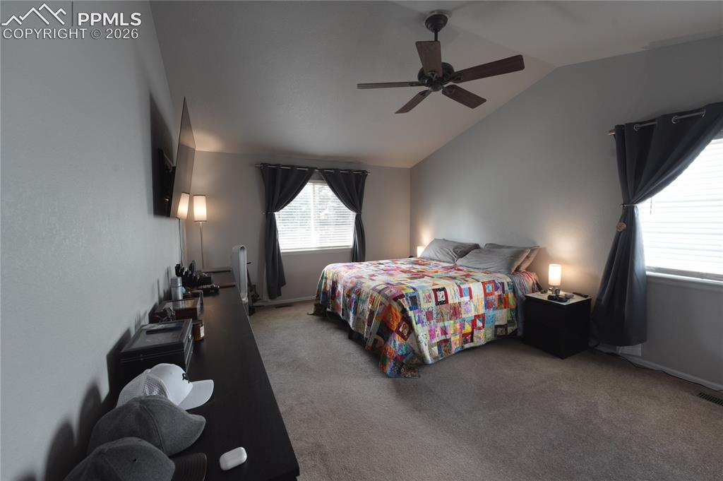 Image 18 of 45: Vaulted ceiling bedroom featuring carpeting, two windows with blinds, a cei