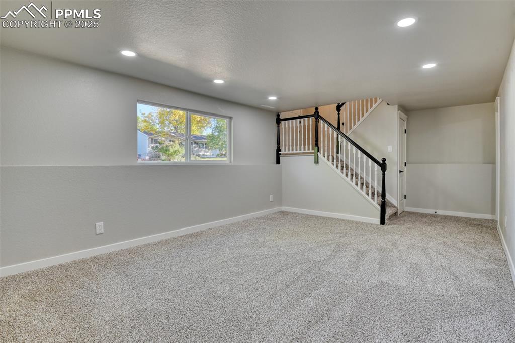 Image 28 of 48: Empty room with light colored carpet, recessed lighting, stairway, and a te