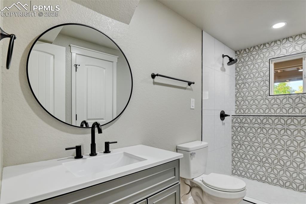 Image 33 of 48: Full bathroom featuring a textured wall, vanity, and a tile shower