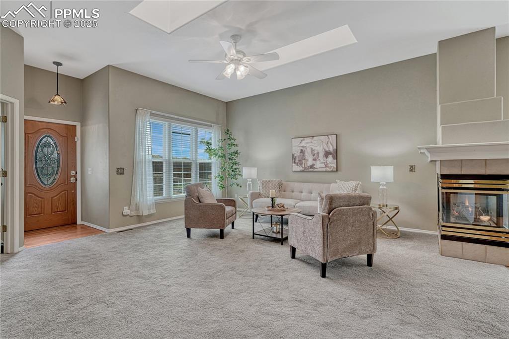 Image 14 of 47: Living room with neutral paint and carpet, 3-sided gas fireplace, and two s