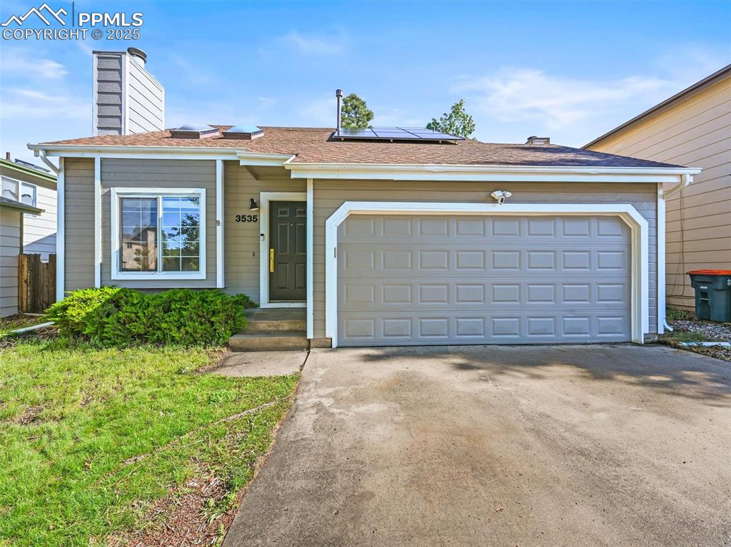 Caption: View of front of house with a chimney, solar panels, concrete driveway, and an attached garage