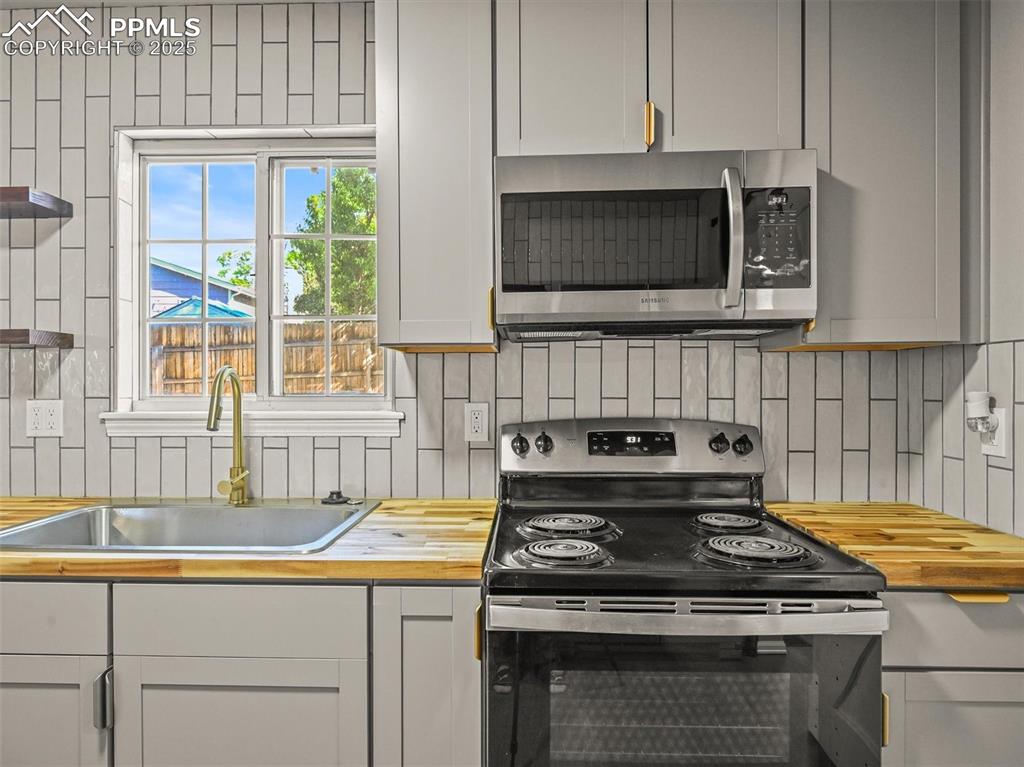 Image 18 of 47: Kitchen with stainless steel appliances, wooden counters, a sink, and decor