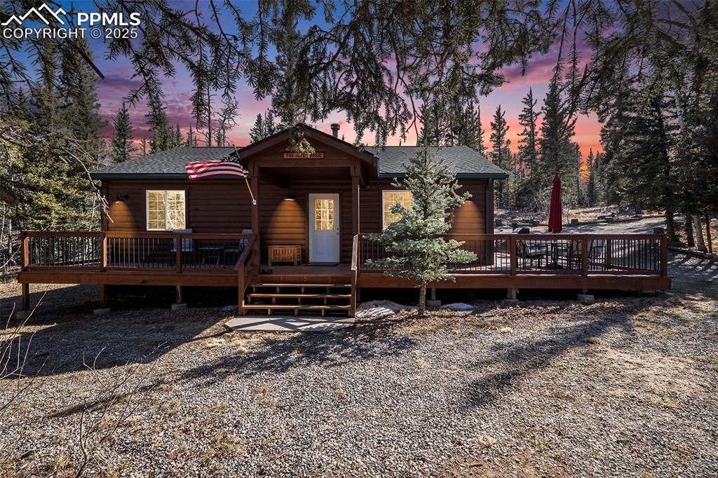 Caption: Chalet / cabin featuring a wooden deck, a shingled roof, and log veneer siding