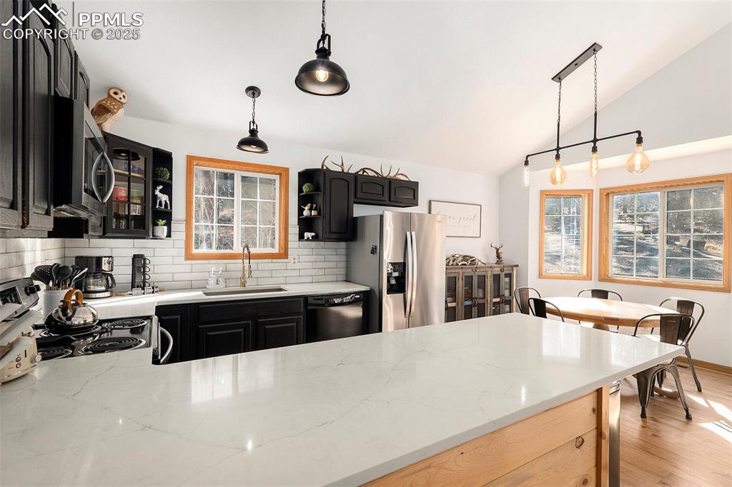 Image 10 of 25: Kitchen with dark cabinets, tasteful backsplash, lofted ceiling, decorative