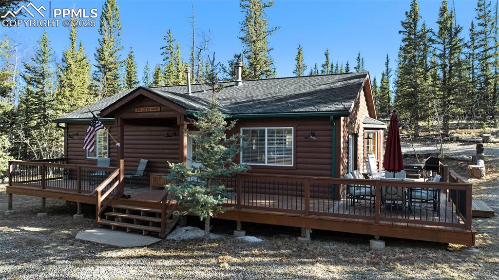 Image 2 of 25: View of front of house with faux log siding, a wooden deck, and a shingled 