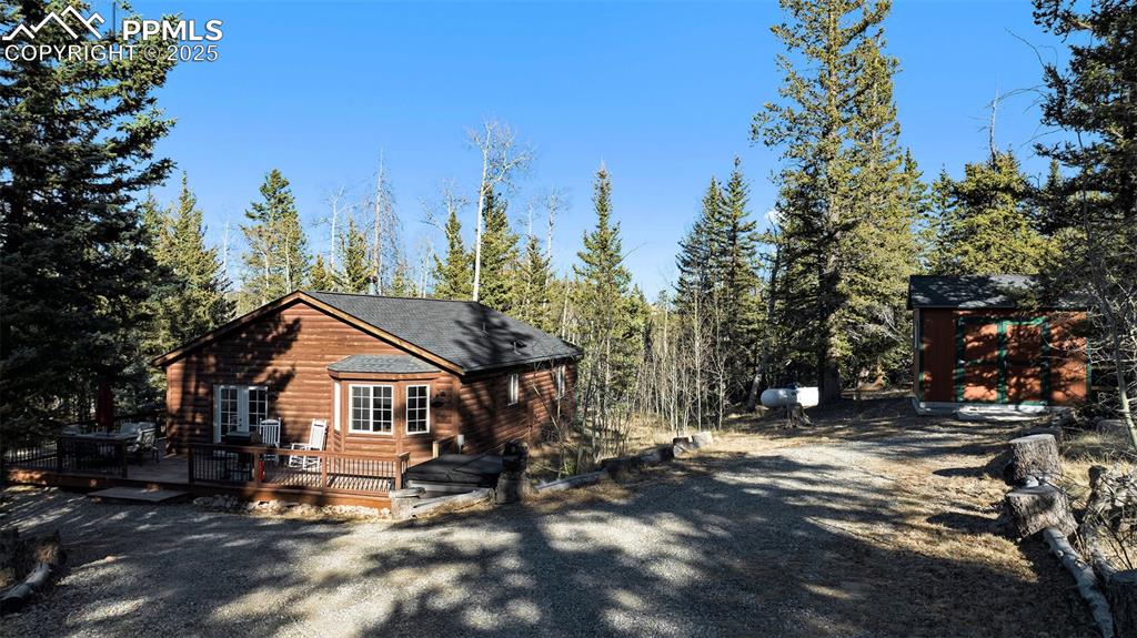 Image 23 of 25: View of front of property with a wooden deck, a storage shed, and log venee