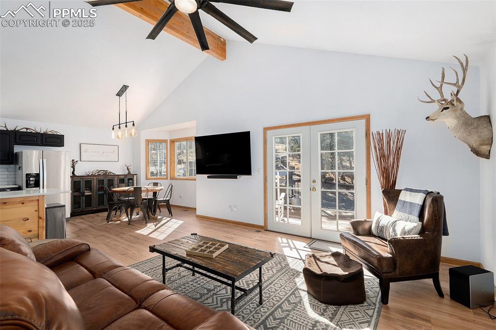 Image 5 of 25: Living area with light wood-style flooring, high vaulted ceiling, beam ceil