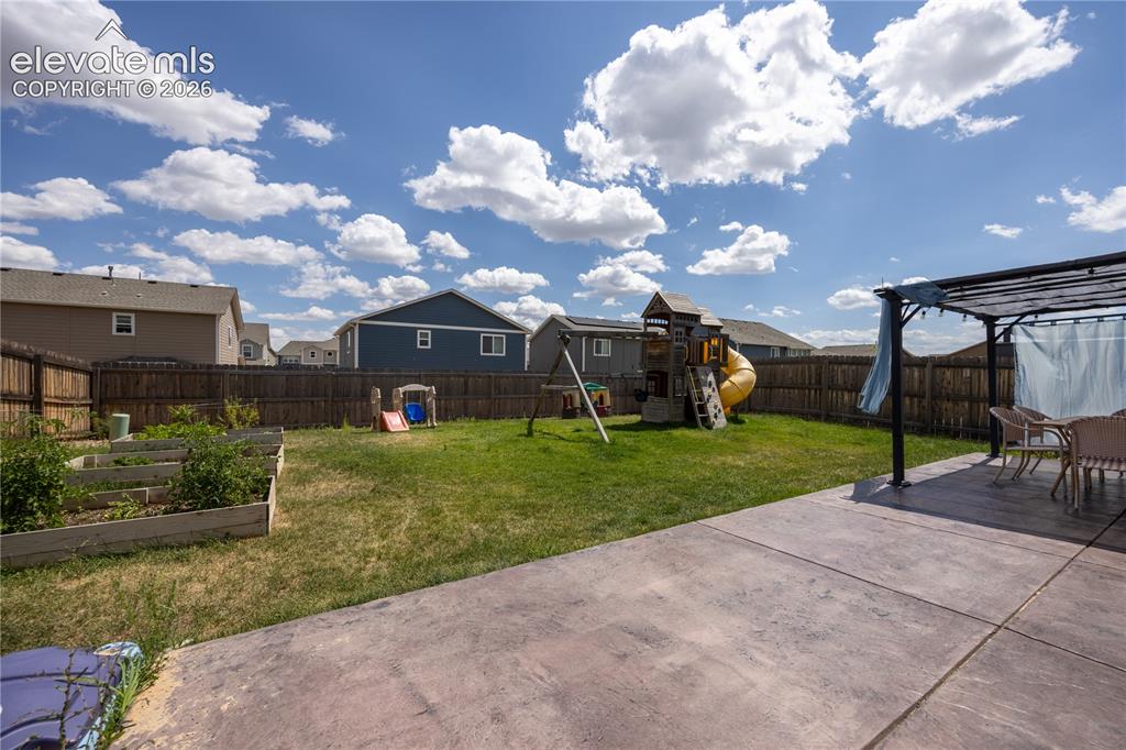 Image 13 of 42: Spacious backyard featuring a concrete patio, a dark-framed pergola, and a
