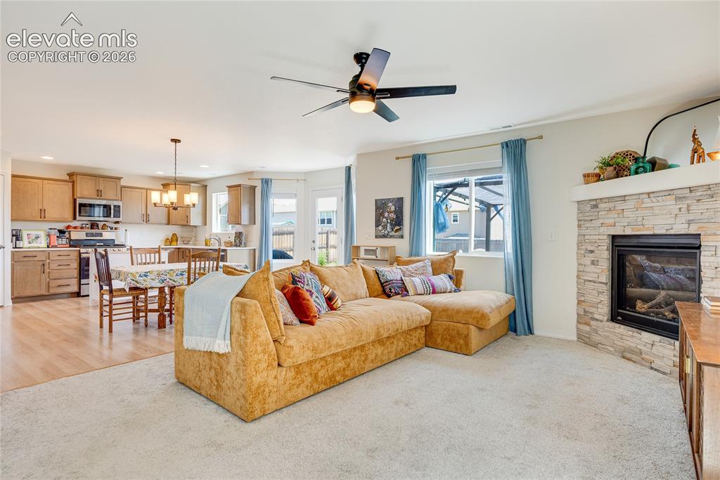 Image 3 of 42: Open-concept living space featuring a stacked stone fireplace, a ceiling fa