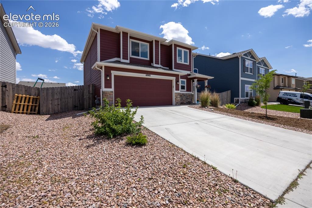 Image 31 of 42: Two-story residence featuring a two-car garage, red siding, and stone accen