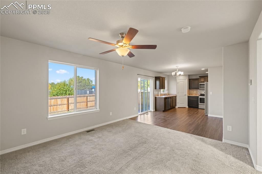 Image 13 of 24: Unfurnished living room featuring dark colored carpet, ceiling fan, and a c